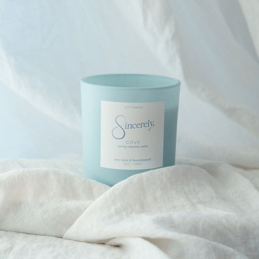 Candle in a light blue vessel and white label on a textured white surface