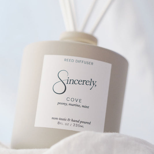 Reed diffuser labeled 'Sincerely' with 'Cove' fragrance on a light background