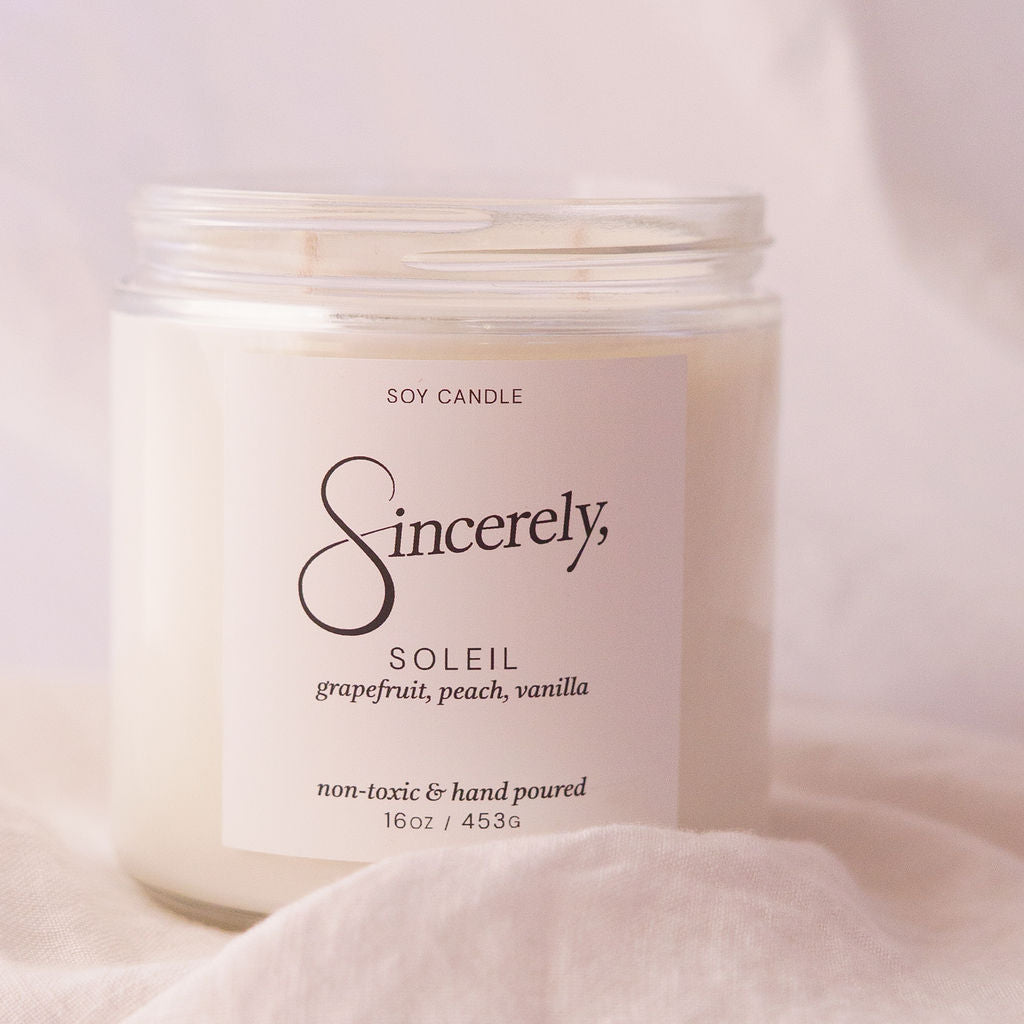 Scented candle jar labeled 'Sincerely Soleil' on a soft pink background