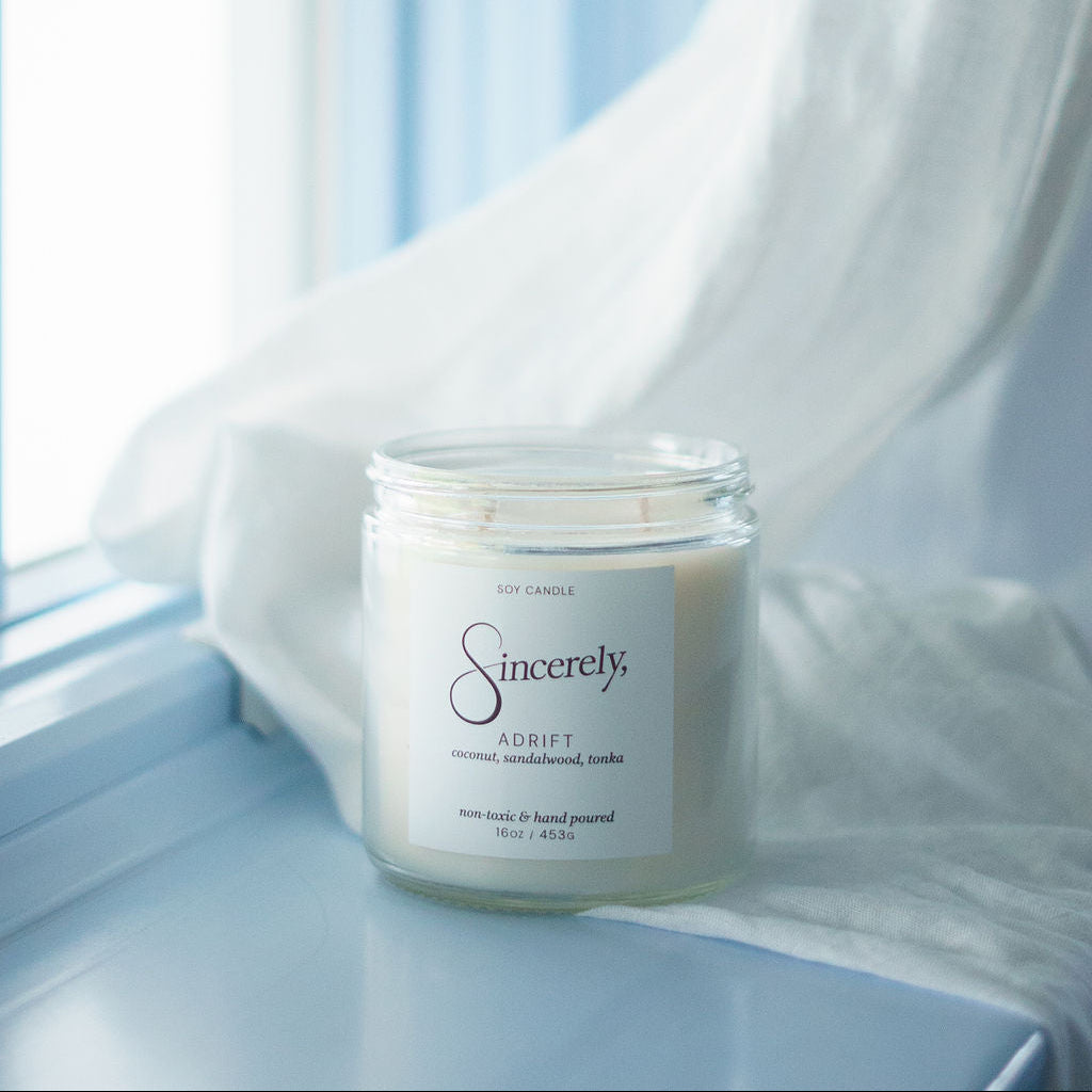 Candle labeled 'Sincerely' on a windowsill with light blue curtains.