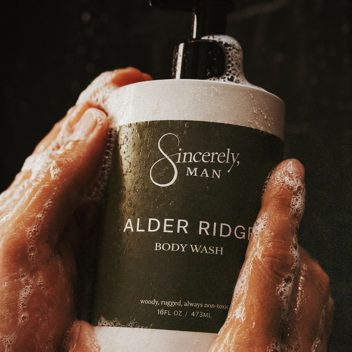 Hand holding a bottle of Sincerely, Man Alder Ridge body wash with a dark background