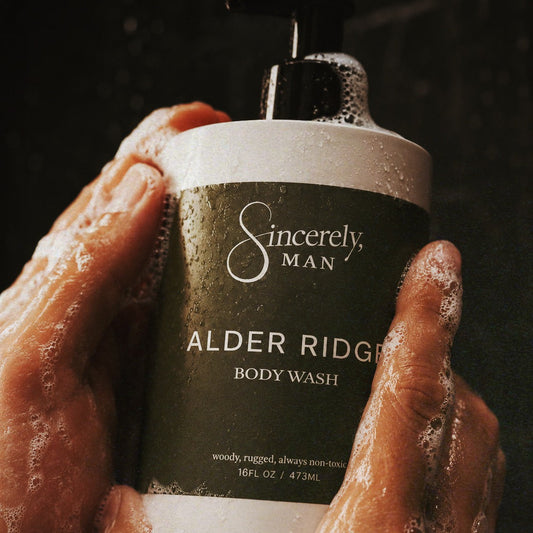 Hand holding a bottle of Sincerely, Man Alder Ridge body wash with a dark background
