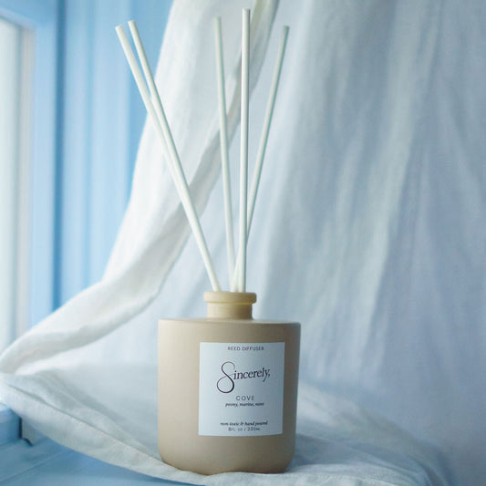 Diffuser with reeds on a light blue surface with sheer white curtains in the background