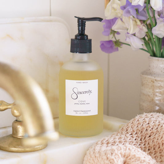 Bottle of 'Sincerely' hand soap on a marble surface with flowers and a towel in the background.