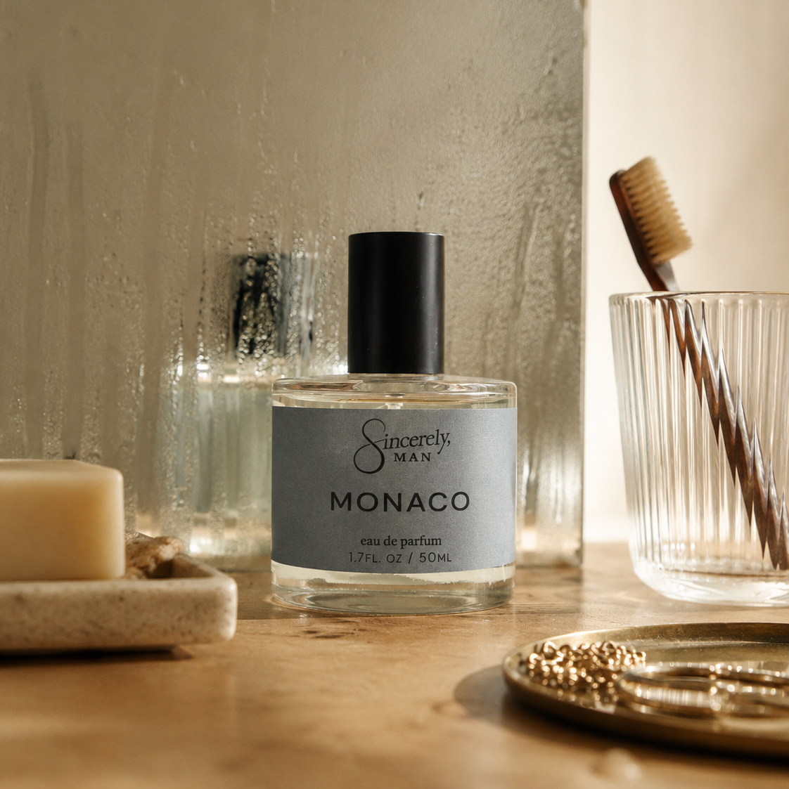 Sincerely Man Monaco perfume bottle on a wooden surface with a candle and brush in the background.