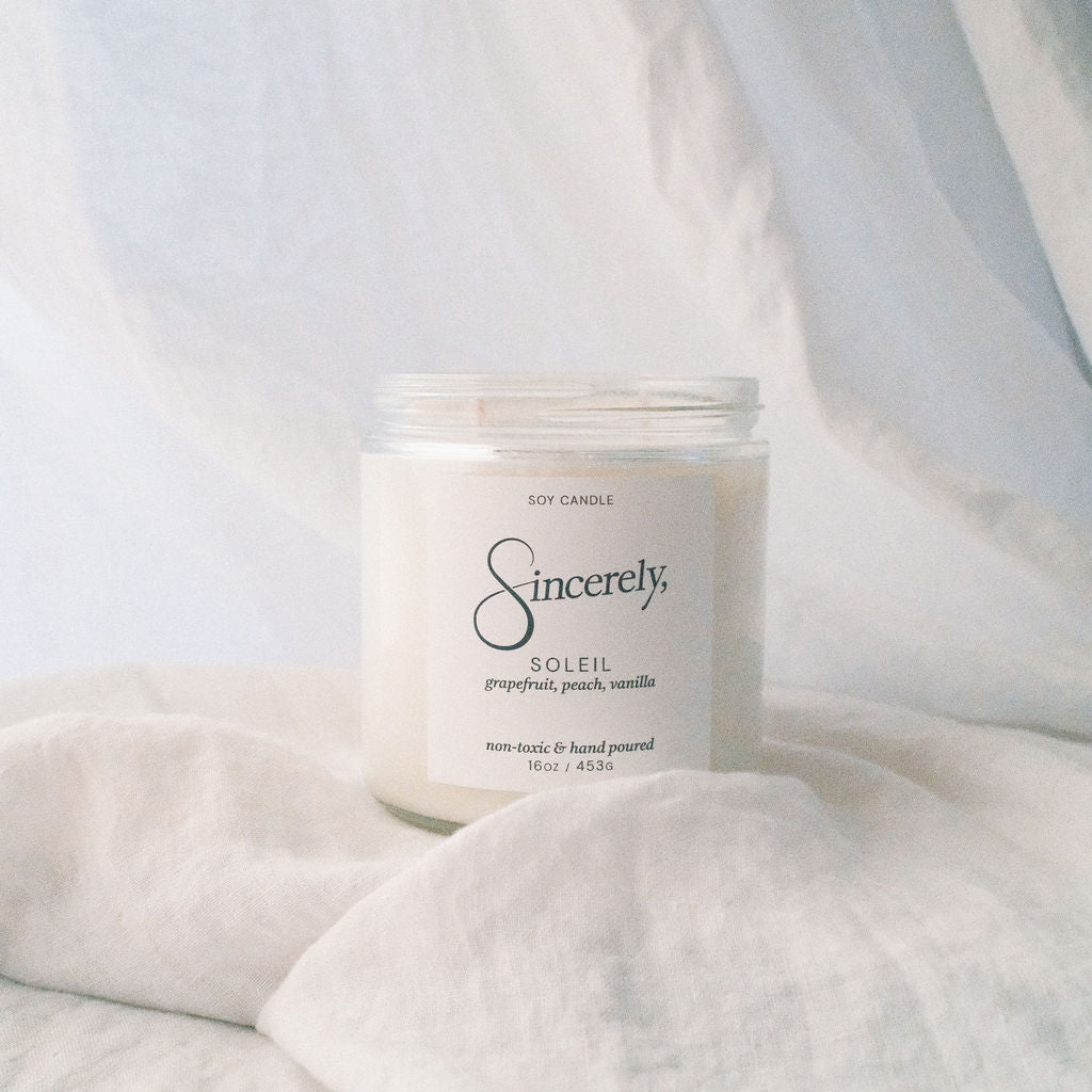 Candle labeled 'Sincerely' on a soft white fabric background