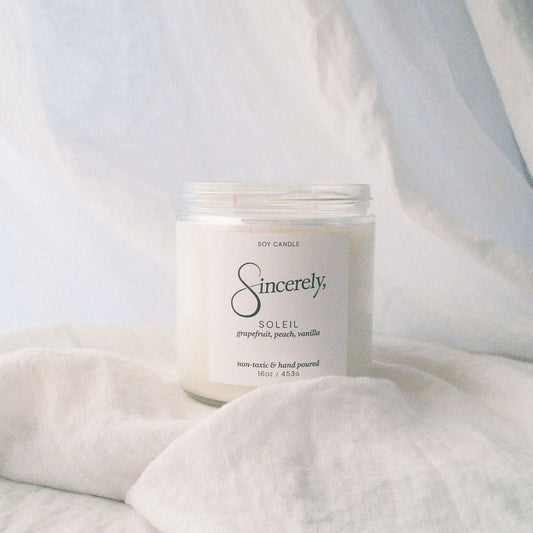 Candle labeled 'Sincerely' on a soft white fabric background