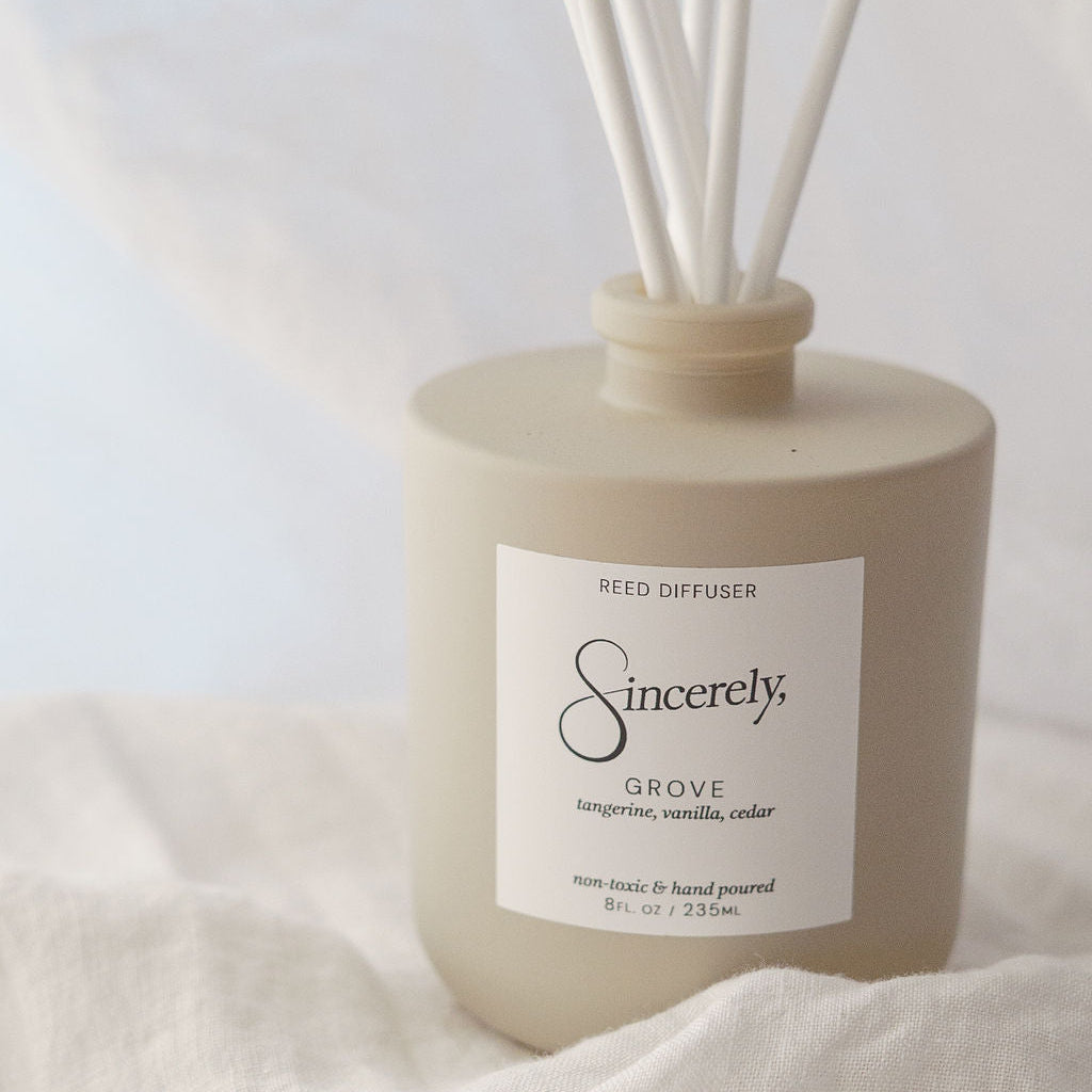 Reed diffuser labeled 'Sincerely' on a light fabric background