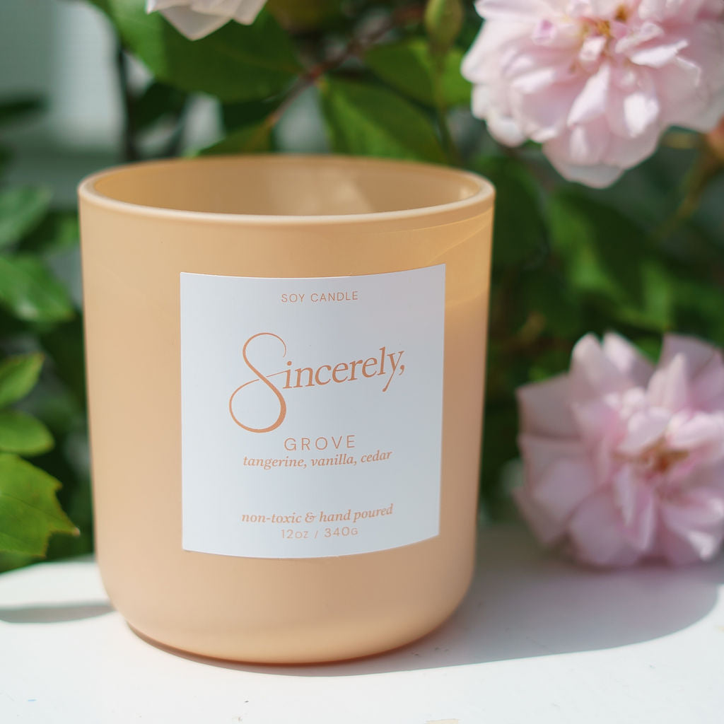 Candle with a label in front of pink flowers