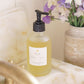 Bottle of liquid soap on a bathroom counter with flowers in the background