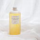 A clear bottle filled with pale golden-yellow liquid, standing upright on draped white fabric. The bottle has a white cap and a white label reading 'AUTUMN LEAVES' with smaller text above and below, and a small script logo near the bottom.