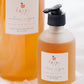 Two bottles of Happy Brown Bag Apple Pie scented hand wash, with one larger bottle in the background and a smaller pump bottle in the foreground on a white textured surface.