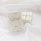 A clear plastic clamshell package of wax melts labeled 'FLOURISH' with several off-white wax cubes visible, placed on soft white fabric.