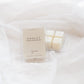 A clear plastic clamshell package of Chalet scented wax melts sits on draped white fabric next to three individual cream-colored wax cubes in a clear tray.