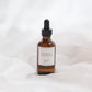 An amber glass dropper bottle with a black dropper cap and a cream label reading 'CHALET' set against a soft white draped fabric background.