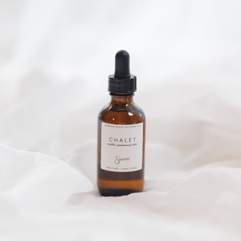 An amber glass dropper bottle with a black dropper cap and a cream label reading 'CHALET' set against a soft white draped fabric background.