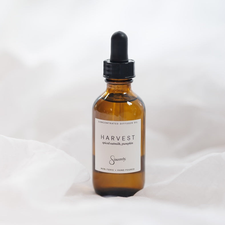 An amber glass dropper bottle of Harvest Spiced Oatmilk, Pumpkin, set against a soft white draped fabric background.