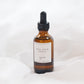 An amber glass dropper bottle with a black cap and a white label reading 'GOLDEN', set against a soft white fabric background.