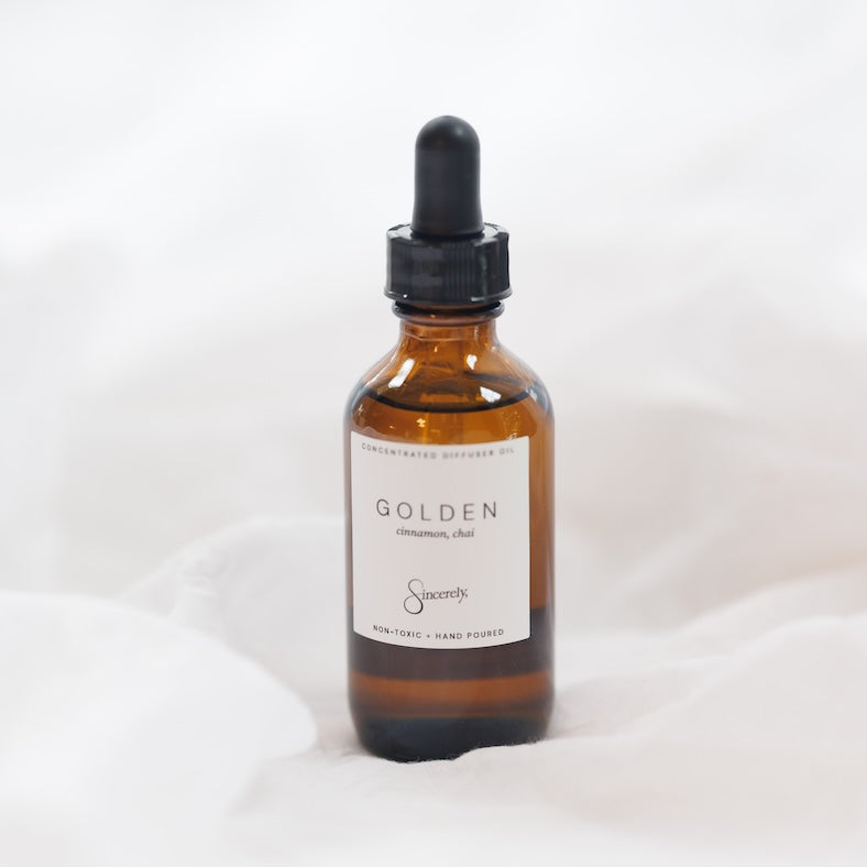 An amber glass dropper bottle with a black cap and a white label reading 'GOLDEN', set against a soft white fabric background.