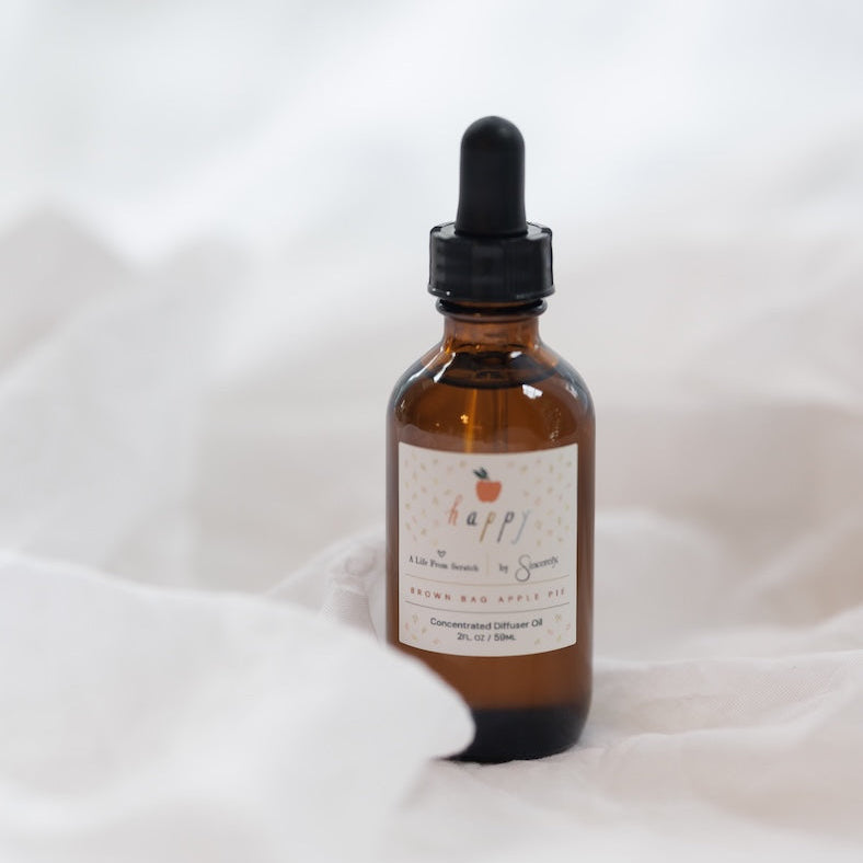 An amber glass dropper bottle with a black rubber bulb and a cream-colored label, set against a soft, draped white fabric background.