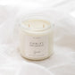 A two-wick soy candle in a clear glass jar with a cream-colored label reading 'CHALET', set against a softly draped white fabric background.