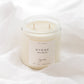 A two-wick soy candle in a clear glass jar with a cream-colored label reading 'HYGGE' and 'Sincerely', styled on draped white fabric.
