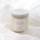 A soy candle in a clear glass jar with cream-colored wax and a white label reading 'GOLDEN cinnamon, chai, set against a soft, draped white fabric background.