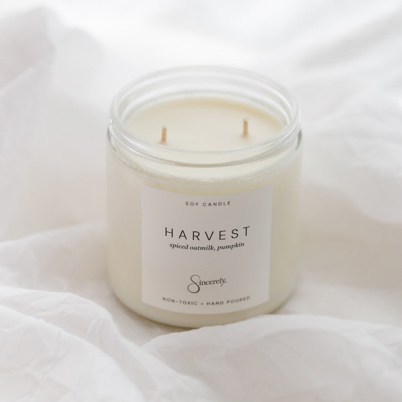 A two-wick soy candle in a clear glass jar with a white label reading 'HARVEST' and the brand 'Sincerey', set on white draped fabric.