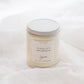 A soy candle in a clear glass jar with a white lid and a cream-colored label reading 'CHALET' set against a soft white fabric background.