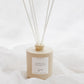 A beige reed diffuser bottle with six white reeds, labeled 'CHALET', set against a soft white draped fabric background.