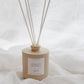 A beige reed diffuser bottle with six natural reed sticks, labeled CHALET, set against a soft white draped fabric background.