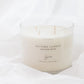 A white soy candle in a clear glass jar with four wicks, labeled 'AUTUMN LEAVES', set against a soft white fabric background.