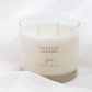 A 4-wick soy candle in a clear glass jar with cream-colored wax, labeled 'HARVEST' and 'Sincerely', resting on white fabric.