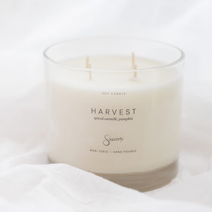 A 4-wick soy candle in a clear glass jar with cream-colored wax, labeled 'HARVEST' and 'Sincerely', resting on white fabric.