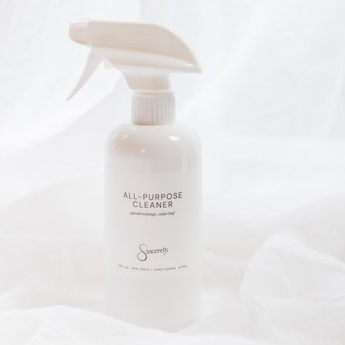 A white spray bottle of All-Purpose Cleaner with a white trigger sprayer, set against a draped white fabric background.
