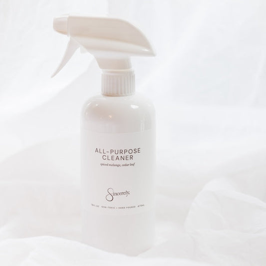 A white spray bottle of All-Purpose Cleaner with a white trigger sprayer, set against a draped white fabric background.