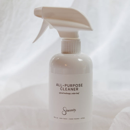 A white spray bottle of All-Purpose Cleaner with a matching trigger sprayer, set against a draped white fabric background.