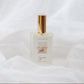 A clear glass perfume bottle with a gold cap and a minimalist white label reading 'CHALET' set against a draped white fabric background.