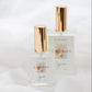 Two clear glass perfume bottles with metallic gold caps, labeled 'Flourish'  set against a draped white fabric background.