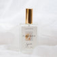 A clear glass perfume bottle with a shiny gold cylindrical cap, labeled 'FLOURISH' by the brand 'Sincerely', set against a soft, draped white fabric background.