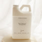 A large white plastic laundry detergent jug labeled 'RETREAT' by Sincerely, placed on a round beige stone slab against a soft white draped fabric background.