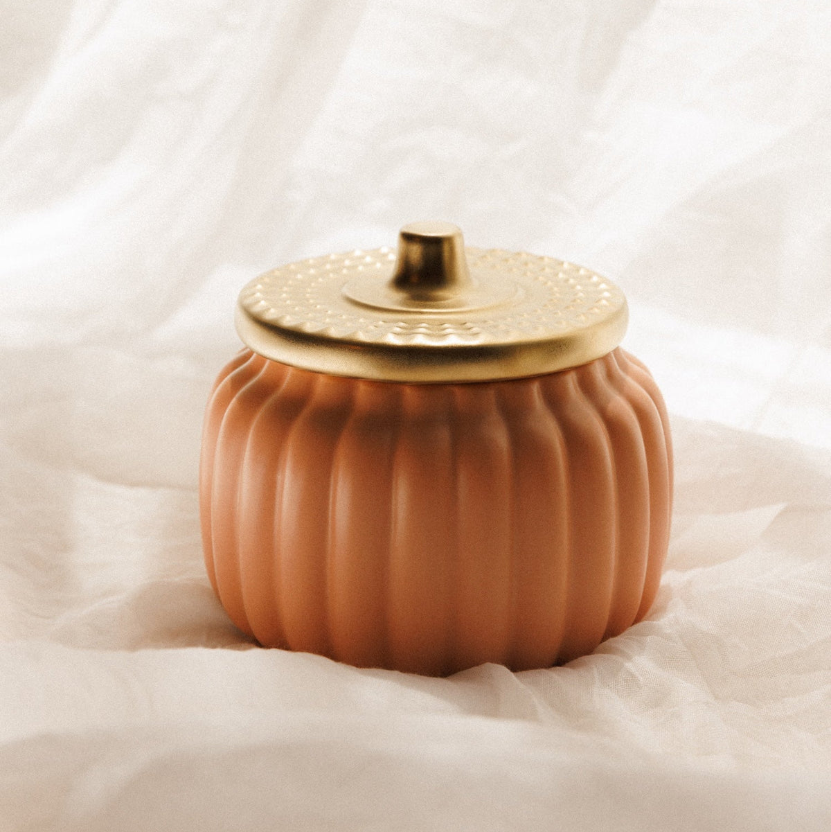 A pumpkin orange ceramic jar with a matching lid, set against a draped white fabric background.