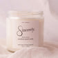 Scented candle jar labeled 'Sincerely Soleil' on a soft pink background