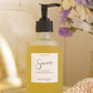 Hand soap bottle labeled 'Sincerely Tranquil' on a surface with flowers in the background