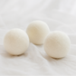 Three off-white wool balls resting on a soft, draped white fabric background.